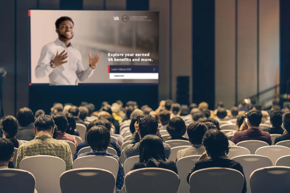 Audience looking at a screen that has a slide with the words Explore your earned VA benefits and more.